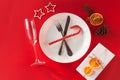 Christmas served dinner, table design on red background. White plate, champagne glass, gift present box, fir, orange, candy cane.