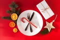 Christmas served dinner, table design on red background. White plate, glass, fork, knife, fir, orange, candy cane and Royalty Free Stock Photo