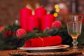 christmas set table, glass goblet and plate with red napkin and branch against the background of red candles