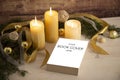 Christmas setting for a book presentation: book with blank cover settled with three lit candles , white organza and gold satin Royalty Free Stock Photo