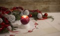 Christmas setting: a red lit candle with cross screen effect on foreground surrounded by pine branches, red baubles, red and white Royalty Free Stock Photo