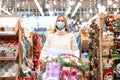 Christmas shopping. Woman with cart shopping in protective medical mask watching Christmas ornament in shopping mall on Holiday Royalty Free Stock Photo