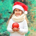 Christmas smiling child little girl in santa red hat with ball near tree Royalty Free Stock Photo