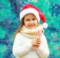 Christmas smiling child little girl in santa red hat with sweet lollipop cane near branch tree