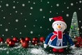 Christmas snowman in red hat and scarf standing with New Year tree and glass ornaments on dark green background Royalty Free Stock Photo