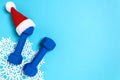 Christmas sport flat lay with dumbbells in red Santa`s hat on blue background