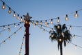 Christmas star and garlands on the background of the evening sky and palm tree. Street Christmas decorations. Royalty Free Stock Photo