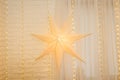 Christmas star on golden lights background on wall in living room. Large paper star glows against the backdrop of New