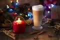 Christmas still life. Glass transparent tall mug of hot cappuccino, cinnamon sticks, red candle, holiday decor with fir