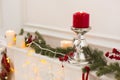 Christmas still life: metal candle holder with red burning candle, white candles, electric garland and green spruce branches