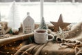 Christmas still life, winter hygge home. Warm cup of tea, christmas decor and lights at window