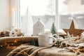 Christmas still life, winter hygge home. Warm cup of tea, christmas decor and lights at window