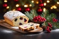 Christmas stollen with holly berries,fir branches and festive decorations on dark table with golden bokeh background.