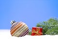 Christmas striped shiny ball with small red gift box on the snow and fir branches. New Year Royalty Free Stock Photo