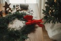 Christmas stylish wreath. Christmas wreath with red bow, cedar branches, vintage bells, pine cones, scissors on wooden table.