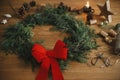 Christmas stylish wreath. Christmas wreath with red bow, cedar branches, vintage bells, pine cones, scissors on wooden table.