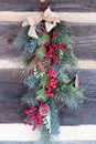 Christmas swag with pine, twigs, red berries, and burlap bow on wood wall