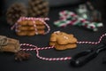 Christmas sweet gift concept: gingerman cookies, pinecones, candycane on black background with red-and-white string. Selective