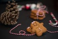 Christmas sweet gift concept: gingerman cookies, pinecones, candycane on black background with red-and-white string. Selective