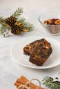 Christmas sweets, slices of fruitcake with dried fruits on a white plate on a light concrete background in Christmas style. Merry