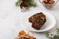 Christmas sweets, slices of fruitcake with dried fruits on a white plate on a light concrete background in Christmas style. Merry