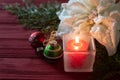Christmas table centerpiece still life with a lighted candle, ornaments, white poinsettia, all on rustic red board background. It