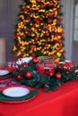 Christmas table decorations with plate, napkin, red tablecloth on backdrop of lights of christmas tree. Decorative composition