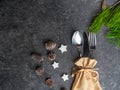 Christmas table place setting, cutlery in burlap bag with festive decorations star, golden bow, pinecone with snow, green branch