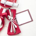 Christmas Table Place Setting in Red, White and Silver with Silverware, a gift, and party cracker on White Cloth Background with r
