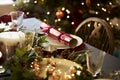 Christmas table setting with a Christmas cracker arranged on a plate with red and green table decorations and a Christmas tree in Royalty Free Stock Photo