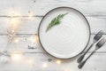 Christmas table setting. Empty plate, garland lights, champagne glass and cutlery. White old wooden table. Top view, flat lay Royalty Free Stock Photo