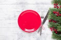 Christmas table setting with empty red plate, gift box and silverware on light wood background. Fir tree branch Royalty Free Stock Photo