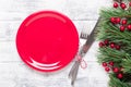 Christmas table setting with empty red plate, gift box and silverware on light wood background. Fir tree branch. Royalty Free Stock Photo