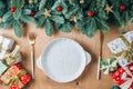 Christmas table setting with empty white ceramic plate, fir tree branch, gold cutlery and gifts on wooden background. Royalty Free Stock Photo