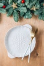Christmas table setting with empty white ceramic plate, fir tree branch and gold cutlery on wooden background. Royalty Free Stock Photo