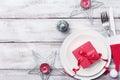 Christmas table setting. Gift box, fir tree, white plate and silverware on rustic table top view. Preparation for holiday dinner.