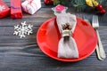 Christmas table setting. Red plate, fork, knife, candle, napkin, gifts branch of a Christmas tree on a dark wooden background Royalty Free Stock Photo