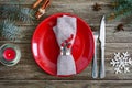 Christmas table setting. Red plate, napkin, fork, knife, branch of a tree on a wooden table. Royalty Free Stock Photo