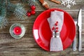 Christmas table setting. Red plate, napkin, fork, knife, branch of a tree on a wooden table. Royalty Free Stock Photo