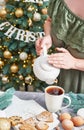 Christmas table setting. Woman pouring tea. Treats and food. Tea set and sweets on background of Christmas tree. Christmastime