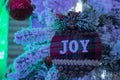 A christmas tartan bauble decoration with the word joy on it hanging on a christmas tree
