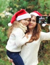 Christmas and technology concept - mother and child taking picture self portrait on smartphone togethe