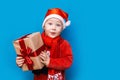 Christmas time. boy with Santa Claus Hat holding christmas gift with red tape and wery surprised face with open mouth Royalty Free Stock Photo