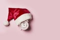 Christmas time.Christmas clock in a Santa Claus hat or cap on a pink background. The minute hand at twelve o Royalty Free Stock Photo