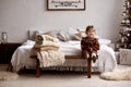 Cute little girl sitting on a big bed in a room with stylish Christmas decorations Royalty Free Stock Photo