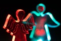 Transparent angel shaped figures illuminated by colorful bulbs isolated on black background