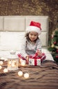 It is Christmas Time! Happy Funny Child Girl Sitting In Bed And Opening The Present On Christmas Morning. Christmas Tree and Light Royalty Free Stock Photo