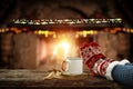 Christmas time, legs in winter socks, mug, book. Space for your text or decoration. Old fireplace wall background. Royalty Free Stock Photo