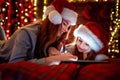 Smiling family mother and daughter in santas hats and pajamas watching funny video or choosing gifts on digital tablet Royalty Free Stock Photo