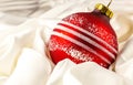 Red shiny christmas toy lies on a white silk cloth.. Christmas decorations and a red ribbon bow isolated on white. Hanging balls, Royalty Free Stock Photo